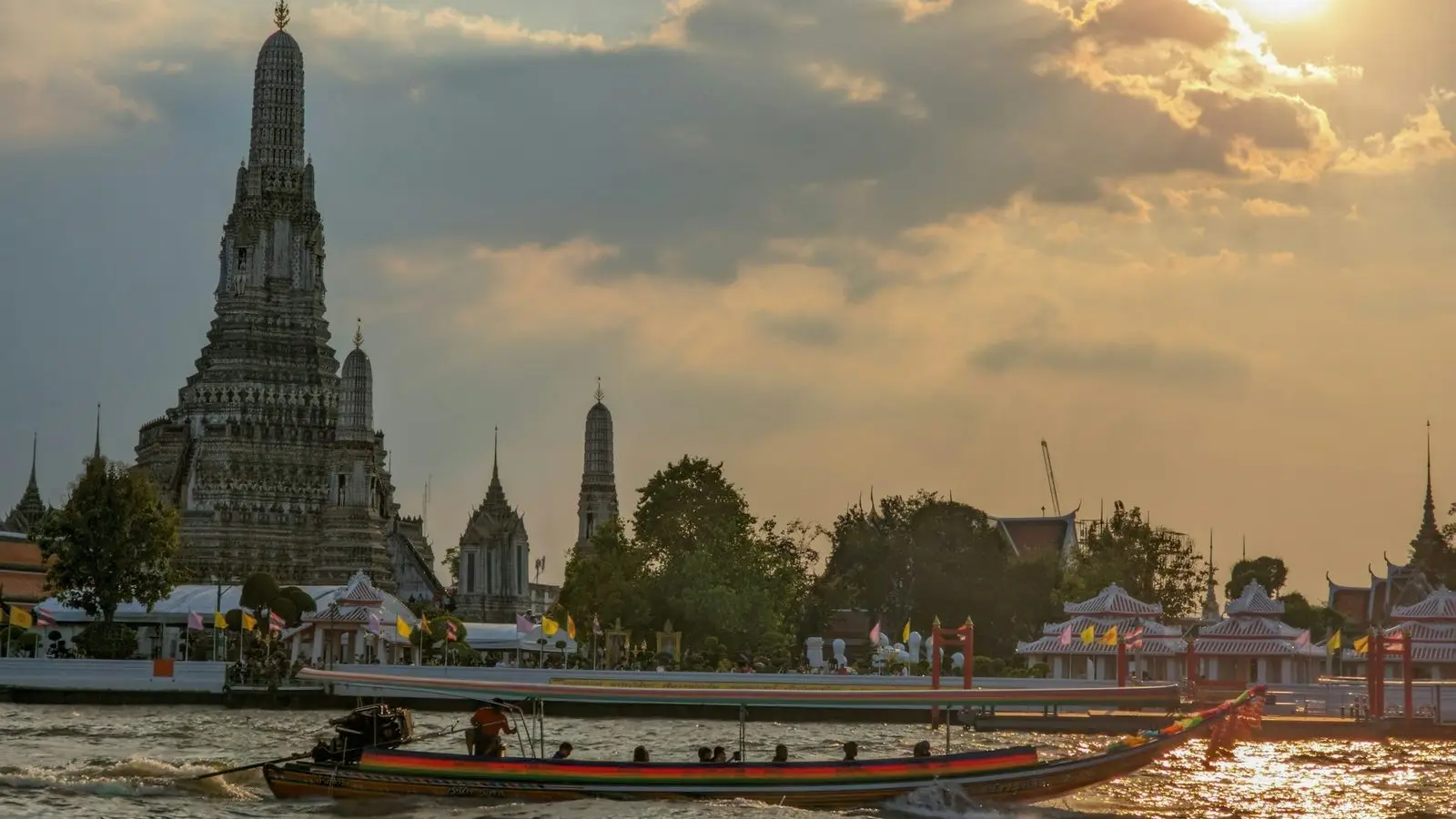 Traditional river express boats gliding gracefully across the waters in front of the illuminated Wat Arun temple