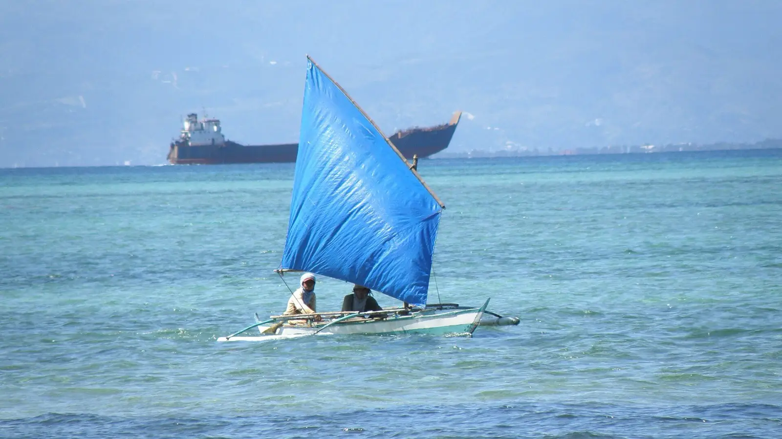 Traditional Philippine outrigger banca boat sailing toward Olango coral reefs for island hopping