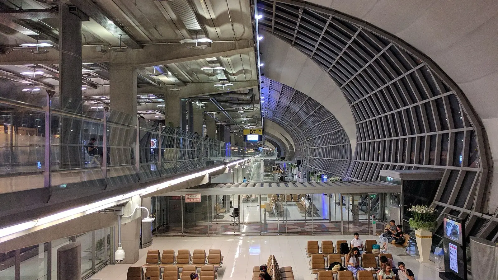 Passengers walking past departure flight boards toward the gates