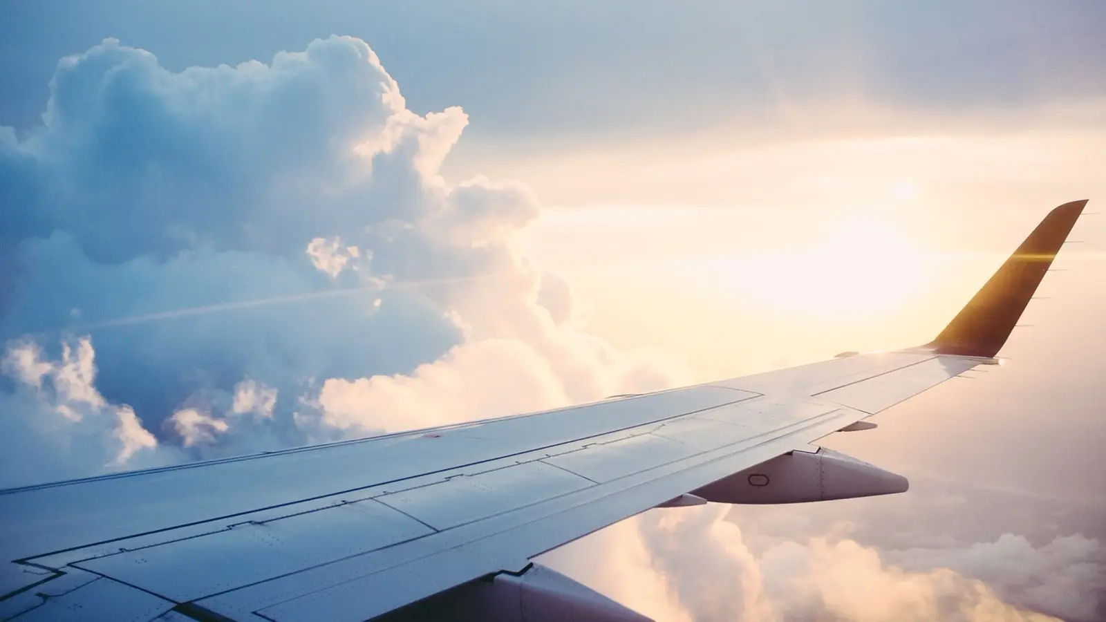 Sweeping cloudscape and aircraft wing tip framed through an economy passenger window