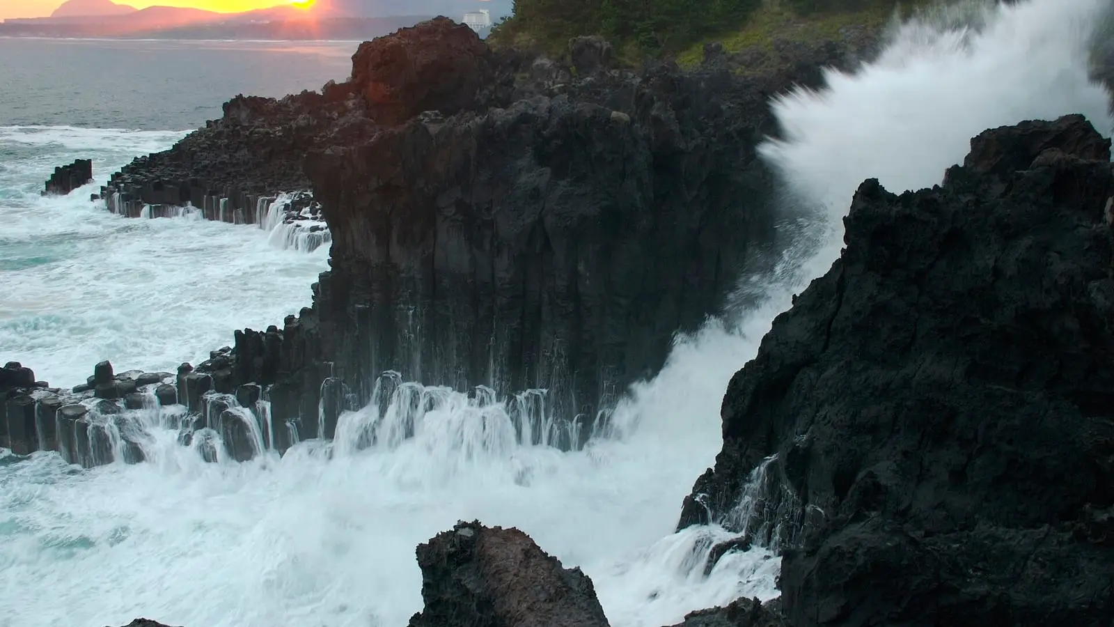Hexagonal volcanic basalt pillars carved by crashing ocean waves along the Jungmun Daepo Jusangjeolli cliffs
