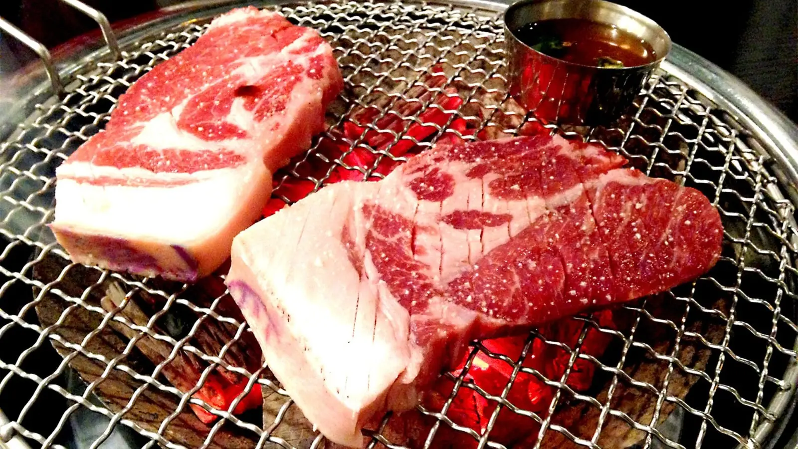 Thick-cut Jeju black pork belly grilled over white charcoal and dipped in bubbling anchovy meljeot sauce