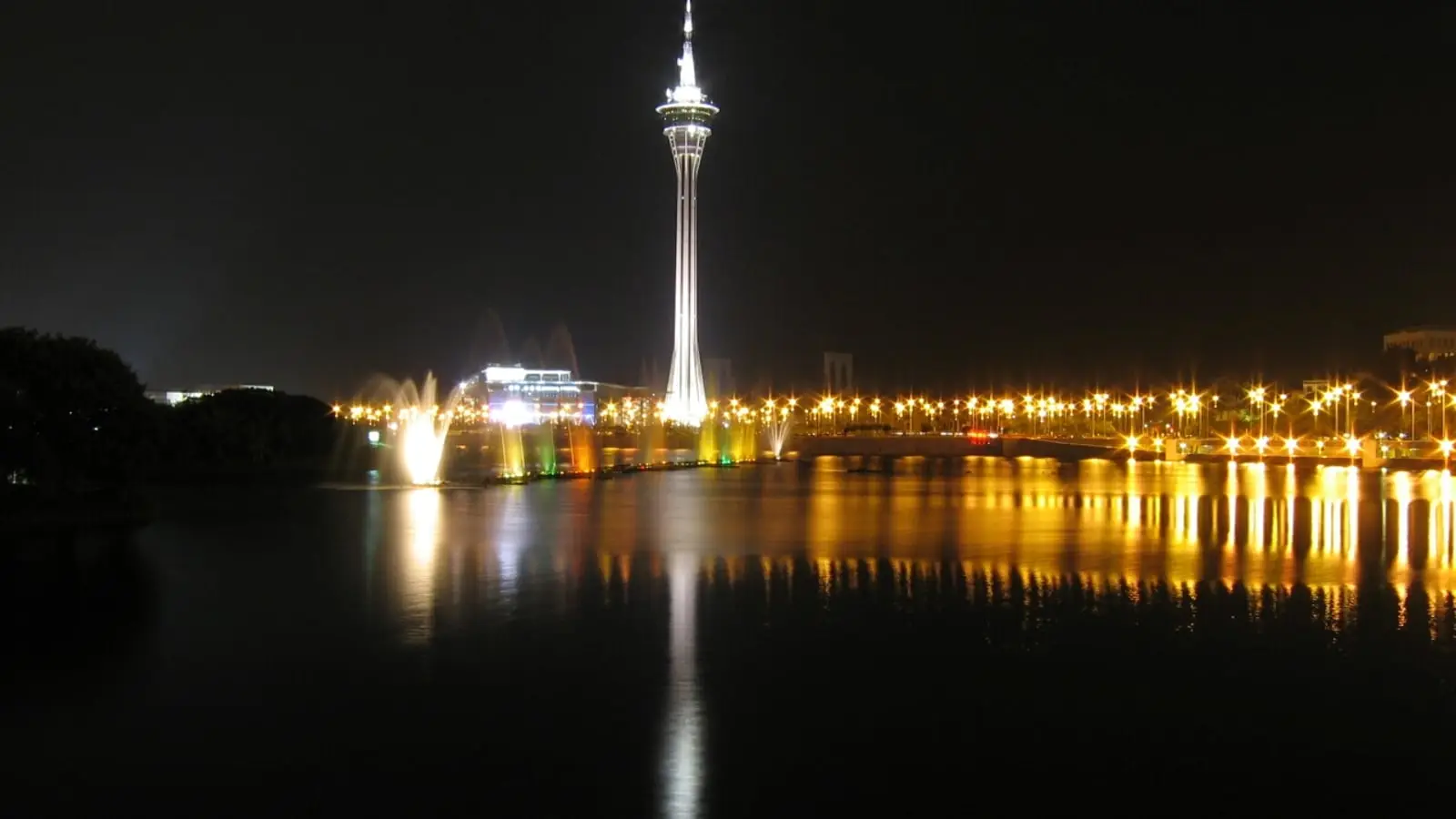 Glowing spire of Macau Tower and peninsula lights mirrored across the waters of Sai Van Lake at night